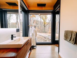 Un baño moderno con un lavabo grande, un mueble de tocador de madera y vistas a un bosque a través de una puerta de cristal.