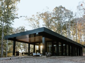 Ein modernes, offenes Pavillon mit Dach, umgeben von Bäumen.