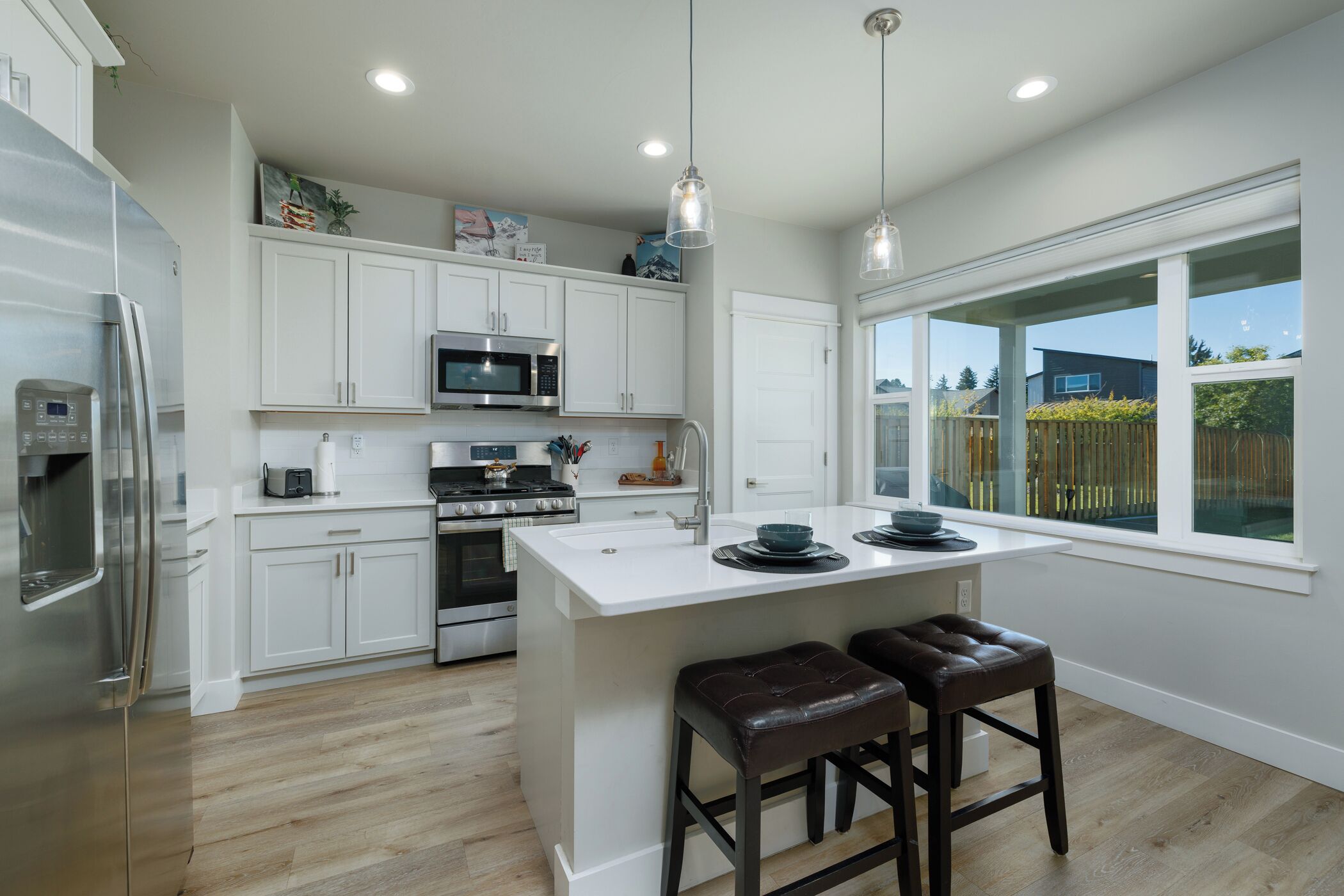 A modern kitchen with white cabinetry, stainless steel appliances, and a large island with bar stools.