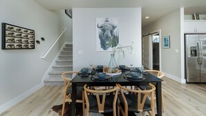 Un coin repas avec une table noire dressée pour six personnes, entourée de chaises en bois. Une grande œuvre d’art représentant un taureau est accrochée au mur et bien visible.