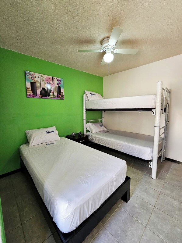 A room with two bunk beds, a ceiling fan, and a green wall with a decorative painting.