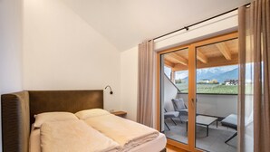 A bedroom with a bed, a nightstand, and a sliding glass door leading to an outdoor seating area with a view of a mountainous landscape. - Apartment 'Linderhof Cima' with Mountain View, Shared Pool and Wi-Fi (Natz)