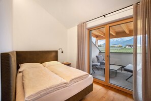 Une chambre à coucher comprenant un lit, une table de chevet et une porte-fenêtre coulissante donnant sur un espace extérieur aménagé avec vue sur un paysage montagneux.