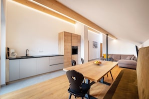 A modern kitchen with wooden cabinets, a dining table, and a sofa in a living area.
