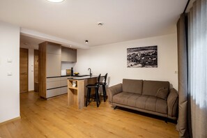 A modern kitchen with wooden cabinets, a dining area with two chairs, a sofa, and a black and white landscape painting on the wall. - Studio Apartment 'Linderhof Nido' with Mountain View, Shared Pool and Wi-Fi (Natz)