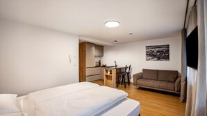 Una habitación con cama, sofá, escritorio con silla y zona de cocina.
