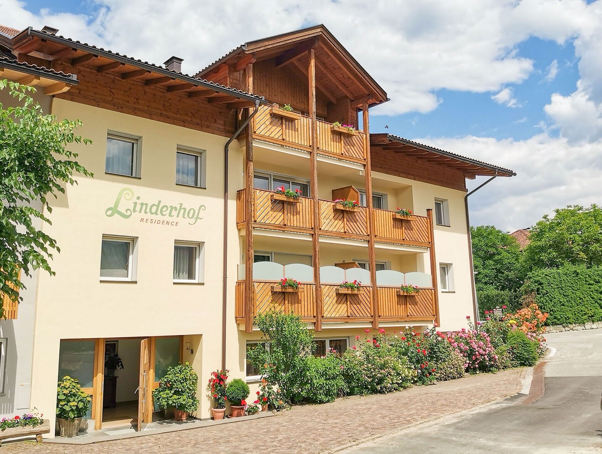 A multi-story building with balconies, a sign reading 'Linderhof RESIDENCE,' and a paved driveway.