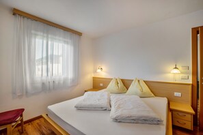 Une chambre d’hôtel avec un lit, une table de chevet en bois, une chaise rouge et une fenêtre avec des rideaux légers.