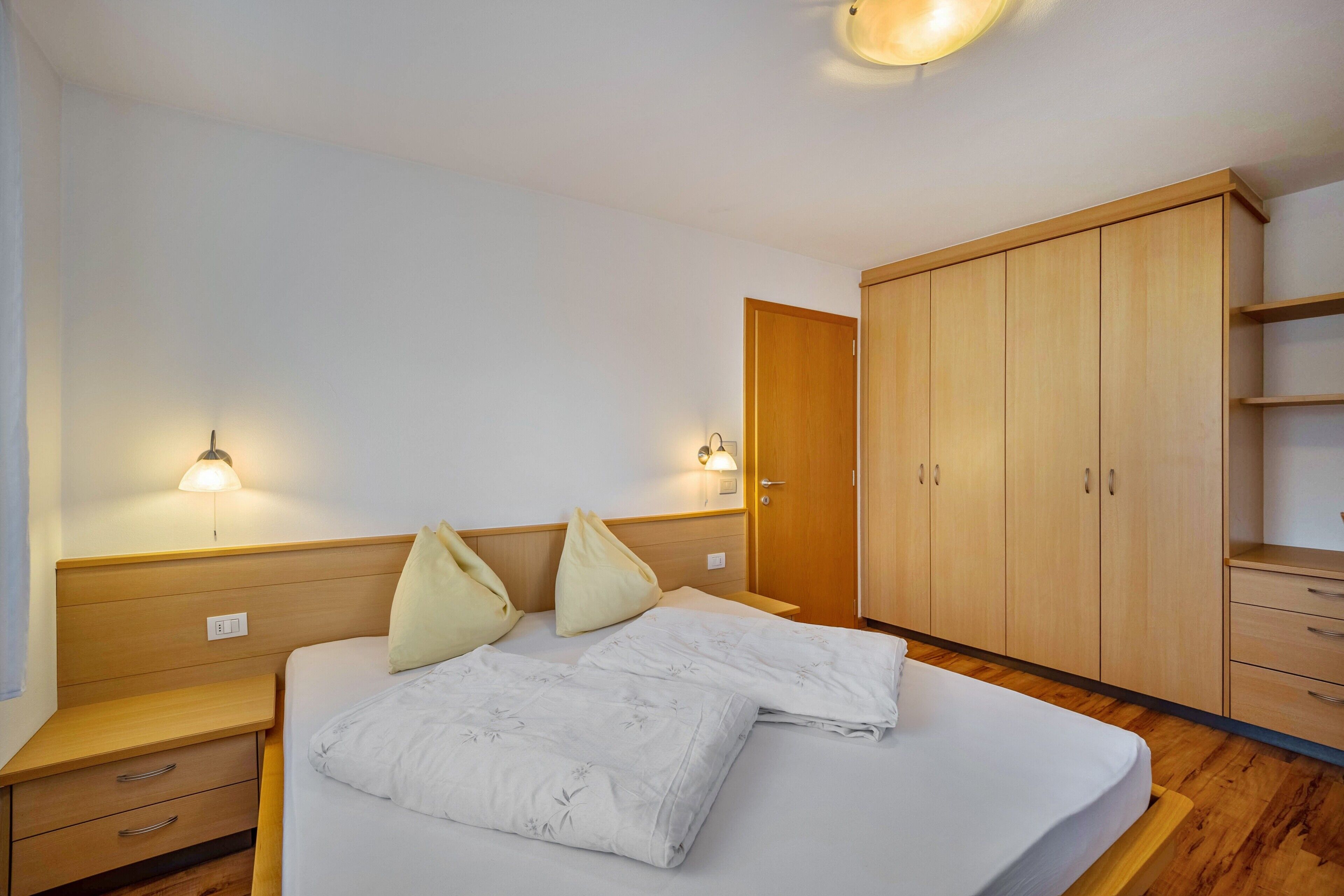 Ein Schlafzimmer mit einem Bett, Nachttischen, einem Kleiderschrank und Wandlampen.