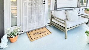 A white door with a decorative glass panel, a bench with cushions, and a welcome mat.