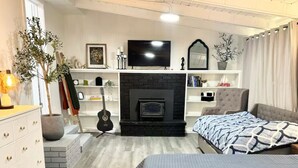 A modern bedroom with a fireplace, a TV, a guitar, and a bed with a blue quilt.