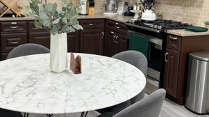 A kitchen with dark wooden cabinets, a white marble table, and grey chairs.