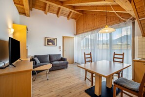 Un plafond en bois, un canapé, une télévision, une table à manger, des chaises et une fenêtre avec des rideaux.