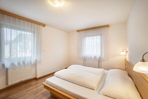 A bedroom with a wooden bed, white bedding, a radiator, and a window with sheer curtains.