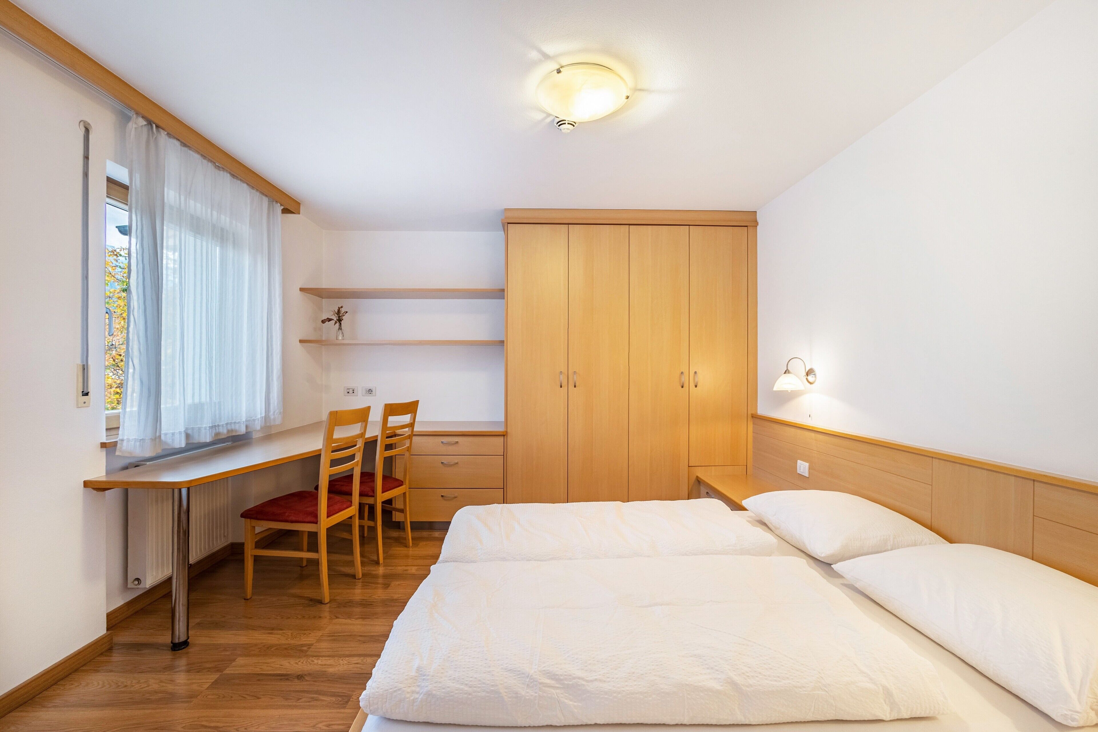 A bedroom with a bed, a desk, a chair, and a wardrobe.