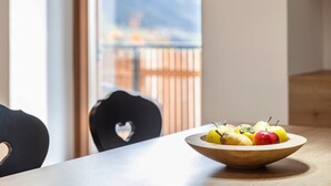 Een houten kom met fruit op een tafel, een stoel in de vorm van een hart, en uitzicht op een balkon met een hekwerk.