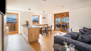A modern kitchen with a wooden island, a dining area with chairs, and a large sliding glass door leading to an outdoor patio. - Apartment 'Linderhof Panorama Terrasse' with Mountain View, Shared Pool and Wi-Fi (Natz)