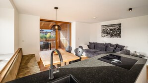 A modern kitchen with a built-in stove, a dining area with a wooden table and chairs, and a gray sofa in the living area. - Apartment 'Linderhof Panorama Terrasse' with Mountain View, Shared Pool and Wi-Fi (Natz)