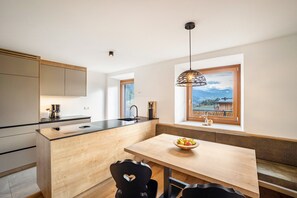 Une cuisine moderne avec un îlot central en bois, une table à manger et une vue sur les montagnes par une fenêtre.