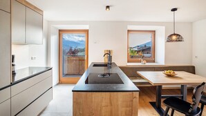 A modern kitchen with a central island, wooden cabinetry, and a view of a mountain landscape through a large window. - Apartment 'Linderhof Panorama Terrasse' with Mountain View, Shared Pool and Wi-Fi (Natz)