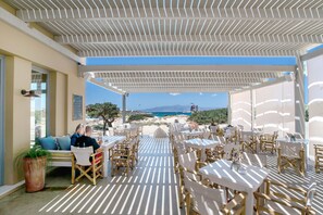 An outdoor dining area with tables and chairs, a view of the beach, and a covered seating area. - Apartment 'Afros Beachfront' with Sea View, Wi-Fi and Air Conditioning (Mikri Vigla)
