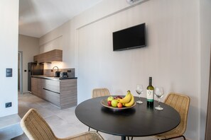 A modern kitchen with a dining area, a flat-screen TV, and a table with fruit and wine glasses. - Apartment 'Afros Beachfront' with Sea View, Wi-Fi and Air Conditioning (Mikri Vigla)