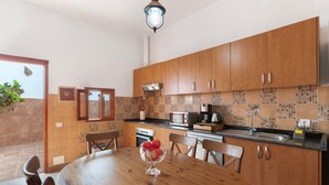 A kitchen with wooden cabinets, a tiled backsplash, a dining table with chairs, and a fruit bowl.