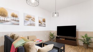 A modern living room with a sofa, coffee table, flat-screen TV, artwork, and potted plants.