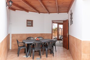 Un patio techado con mesa y sillas, techo de madera y una puerta que da al exterior.