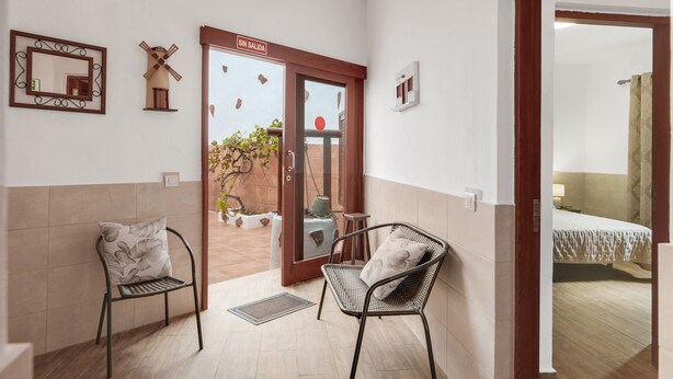 A hotel room with a bed, a bathroom, a balcony with a windmill decoration, and a door with a 'SIN SALIDA' sign.