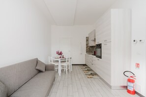 Un espacio habitable compacto con sofá, una mesa de comedor con sillas, una zona de cocina y un extintor.