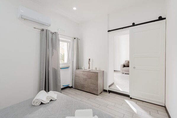 A modern hotel room with a bed, a dresser, a sliding door, and an air conditioning unit.