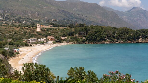 Un paysage côtier avec une plage, des bâtiments et des montagnes.