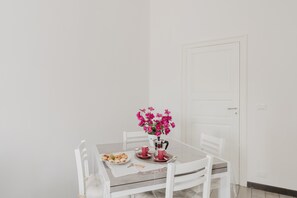 Una mesa de comedor con sillas, un jarrón de flores y una bandeja con comida y bebidas.