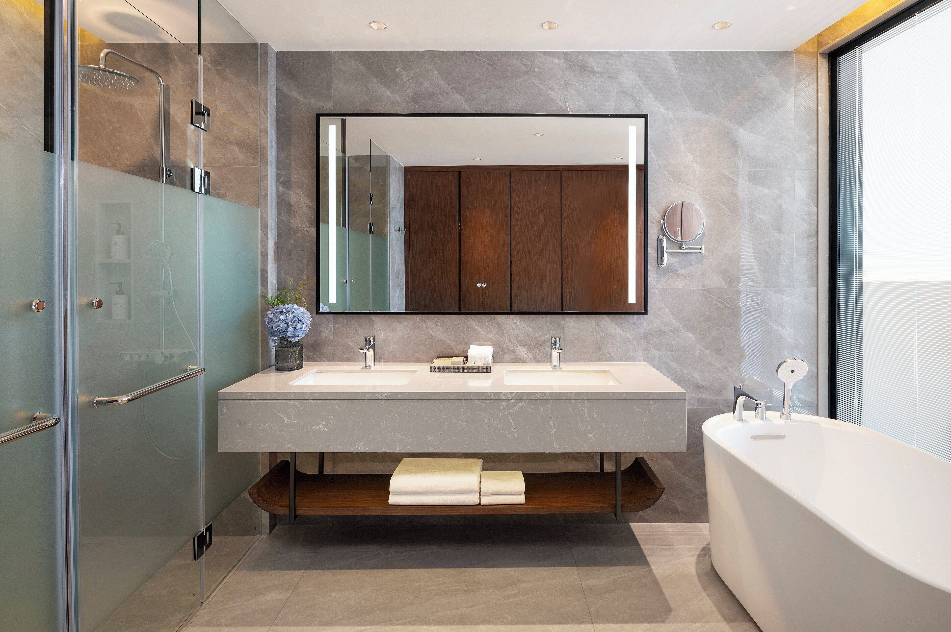 A modern bathroom with a large mirror, two sinks, a bathtub, and a glass-enclosed shower.