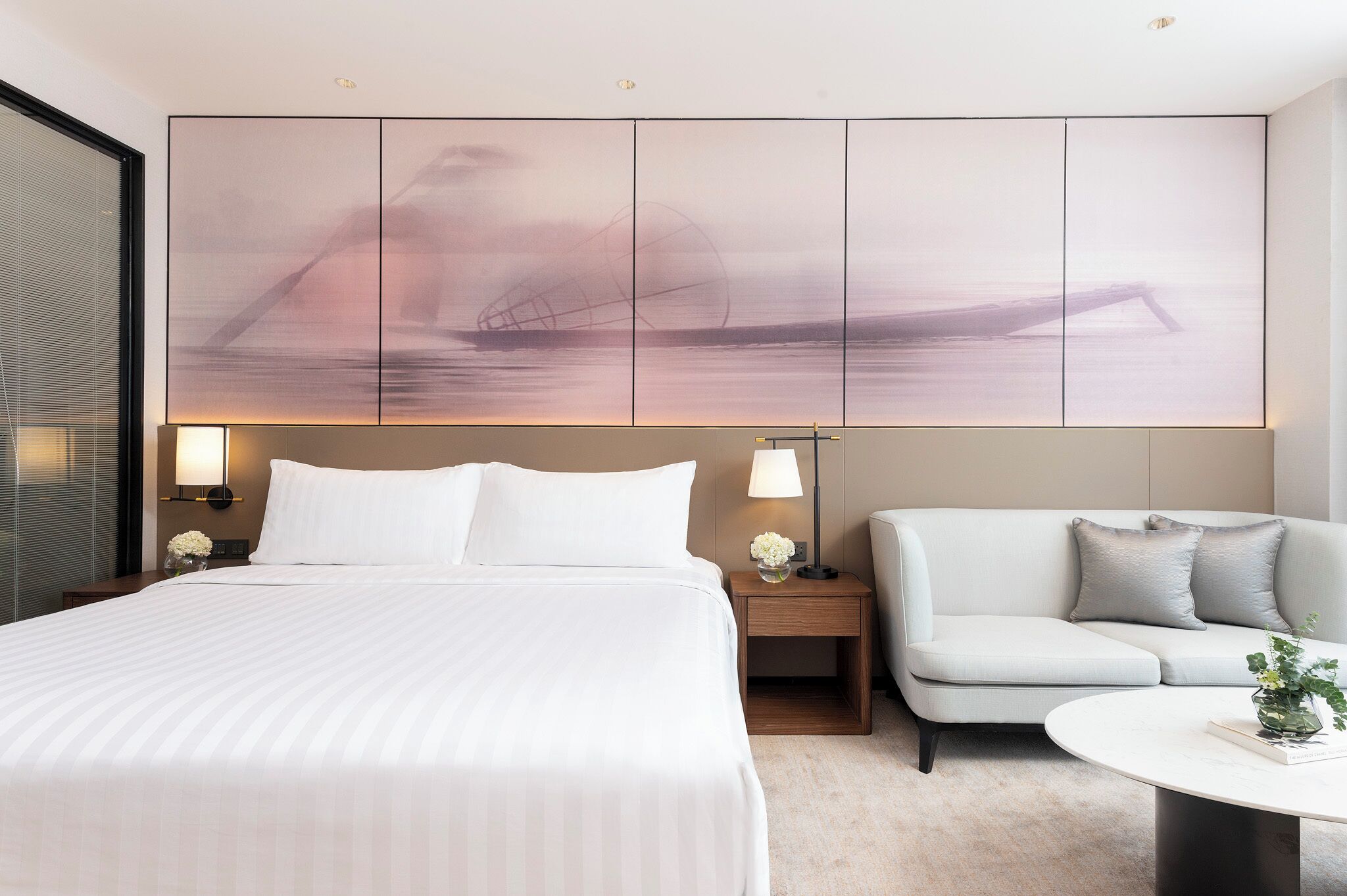 Una habitación de hotel con una cama grande, un sofá, una mesita y una obra de arte colgada en la pared.