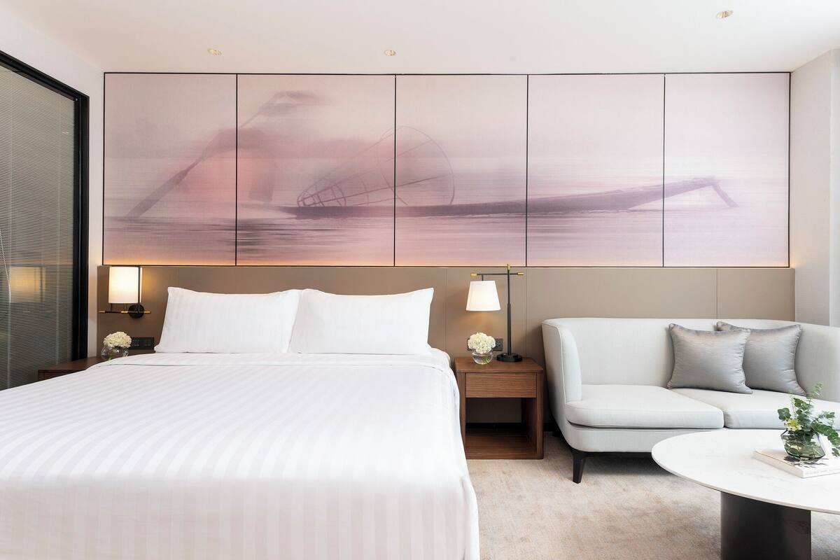 A hotel room with a large bed, a sofa, a small table, and a wall-mounted artwork.