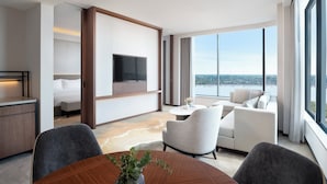A modern hotel room with a large bed, a TV mounted on the wall, a seating area with a sofa and chairs, and a view of the city through large windows. - Amari Vientiane Laos (Vientiane)