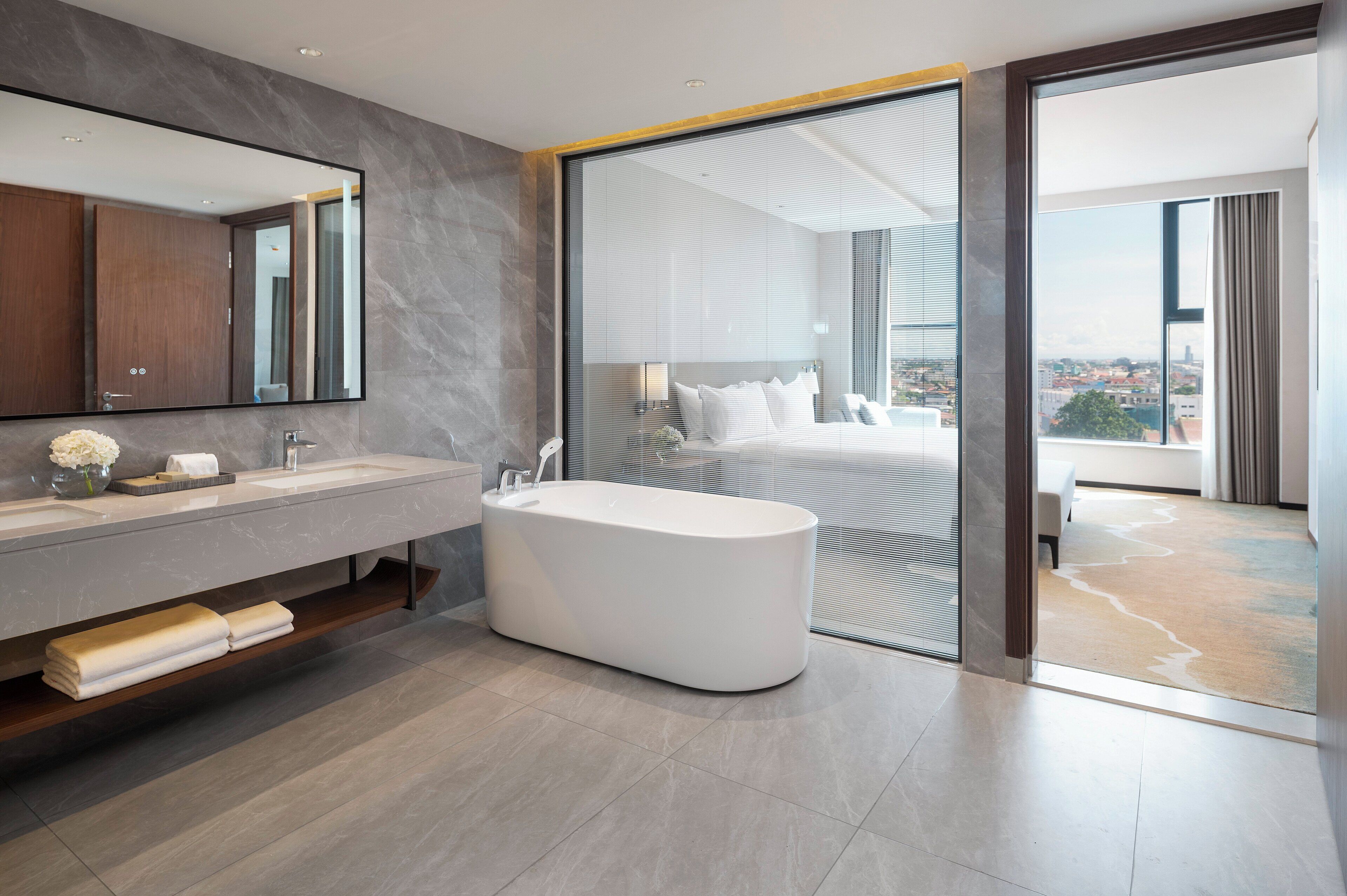A modern bathroom with a large mirror, a bathtub, and a view of a cityscape through a sliding glass door.