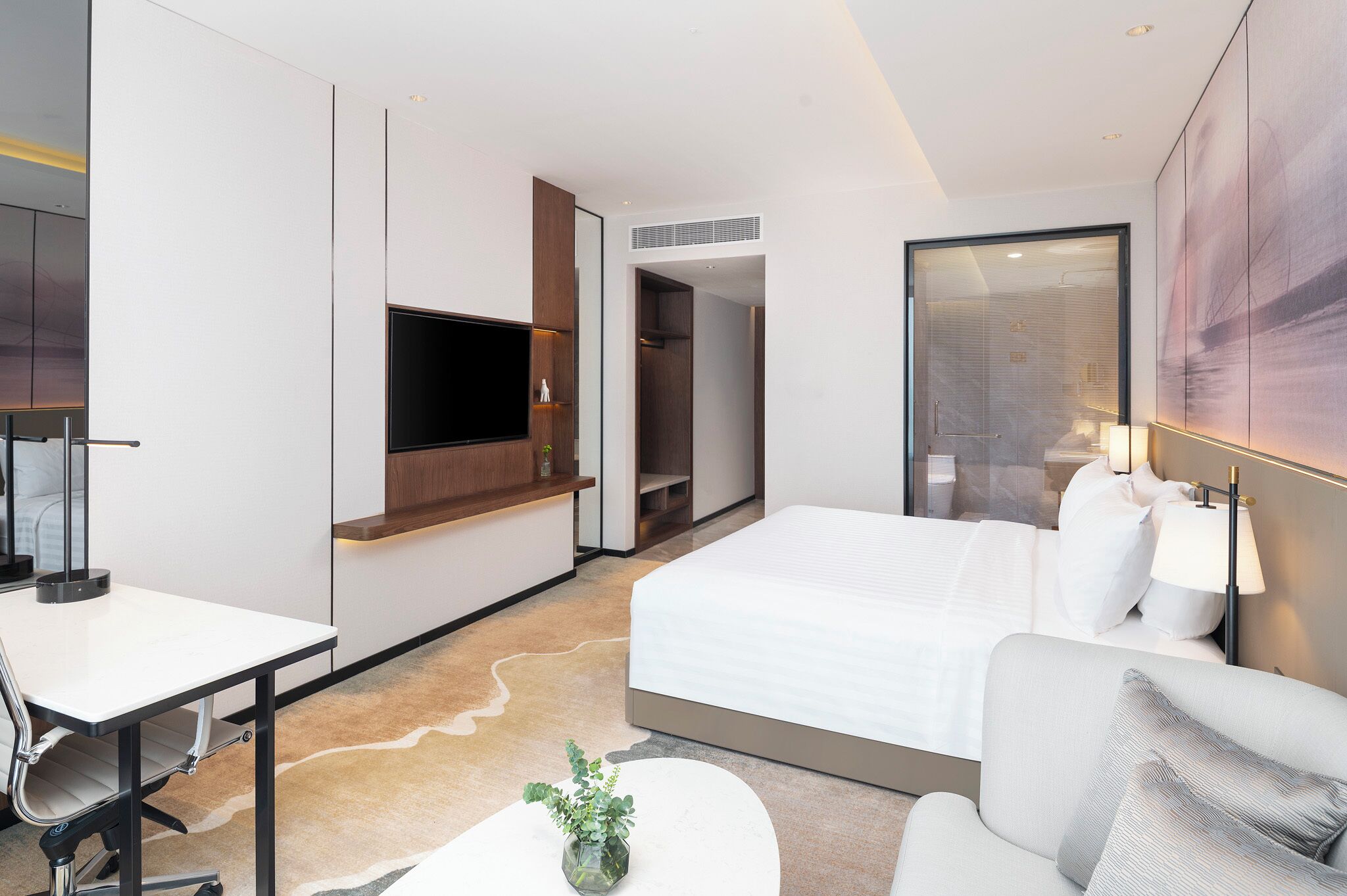 A modern hotel room with a bed, desk, chair, TV, and a large window.