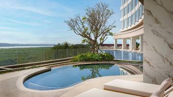 A swimming pool with a curved edge, surrounded by lounge chairs and a tree.