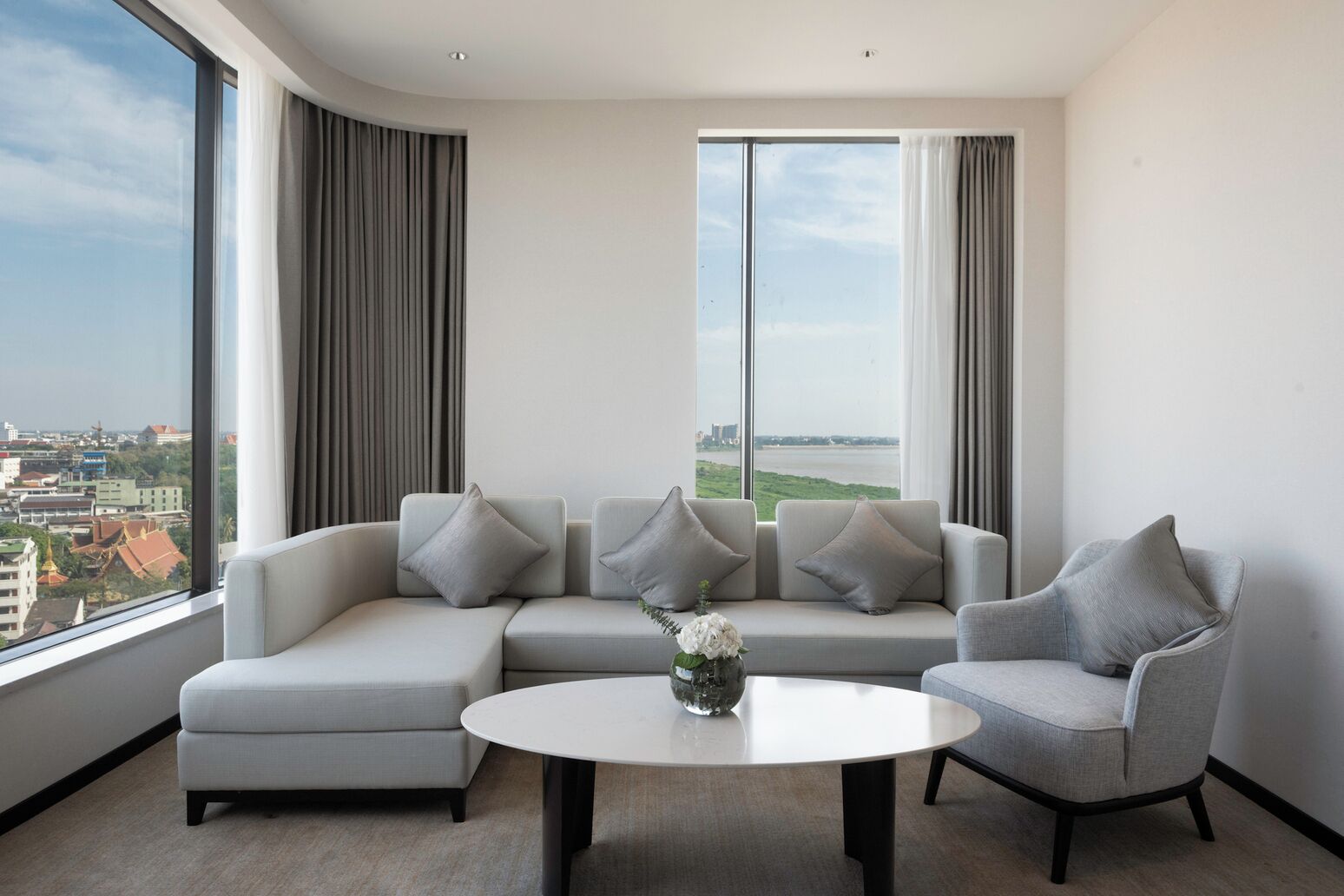 Una sala moderna con un sofá seccional, dos sillones, una mesa redonda y un ventanal con vistas a la ciudad.
