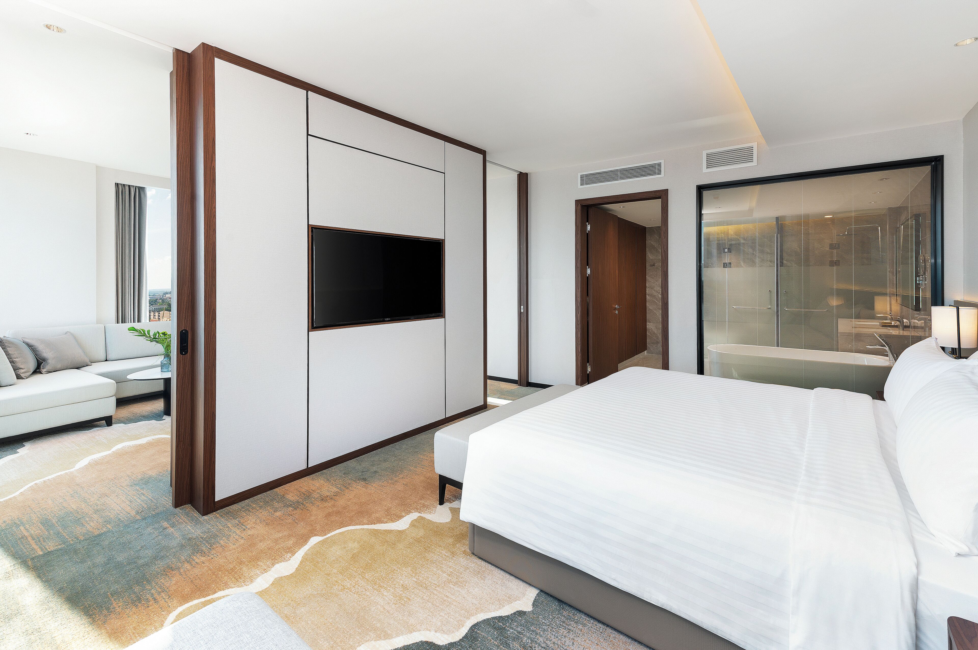 Quarto de hotel moderno com cama grande, televisão de tela plana, sofá e box de chuveiro em vidro.