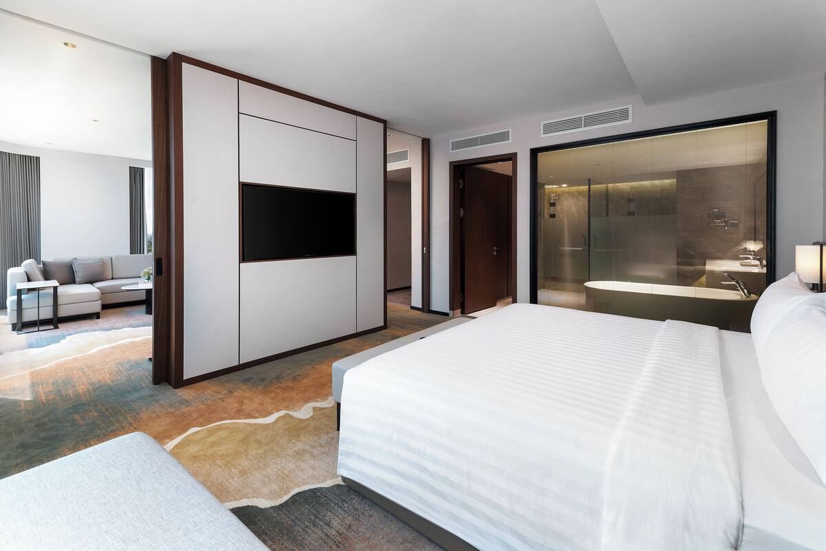 A modern hotel room with a large bed, a flat-screen TV, a sofa, and a bathroom with a glass shower enclosure.