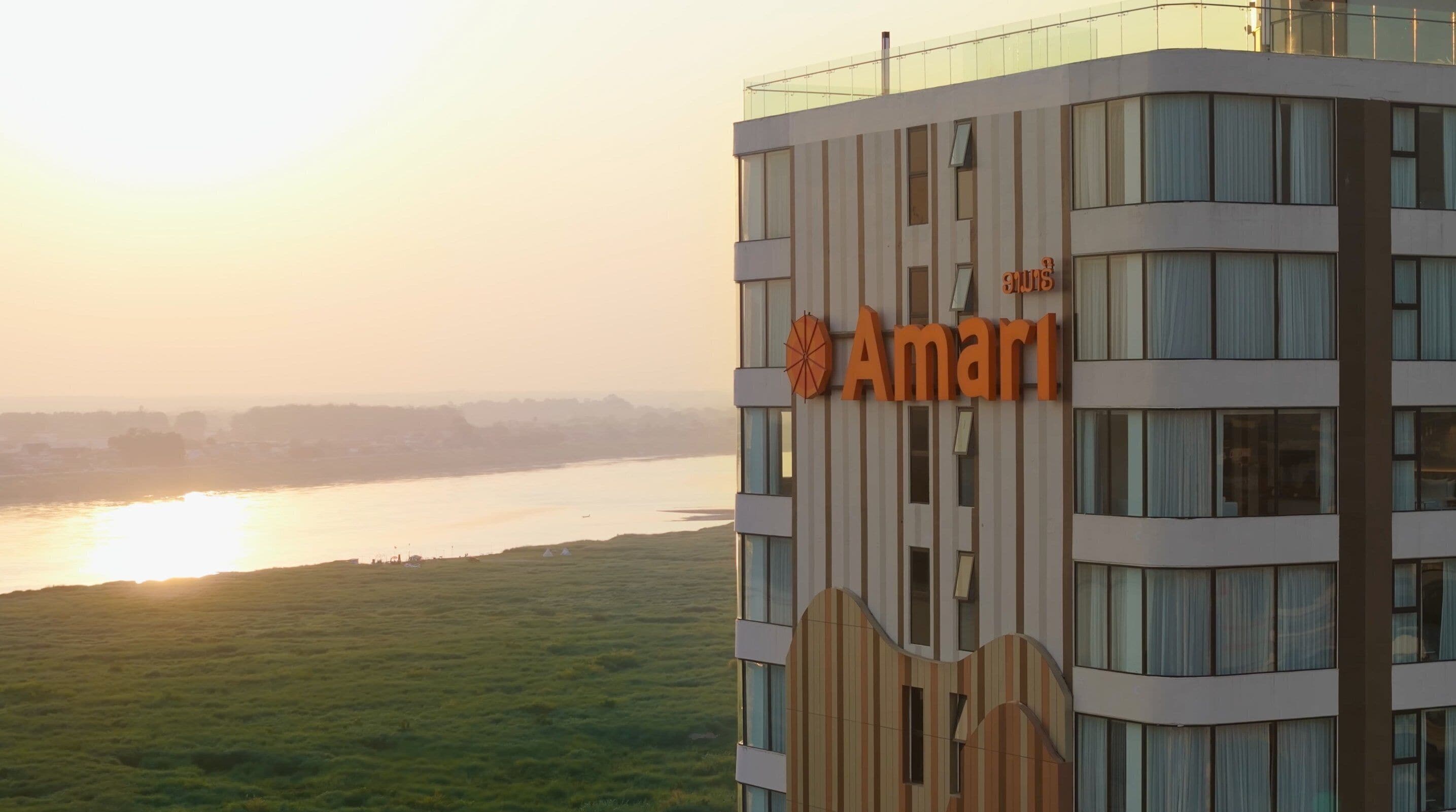 En moderne bygning med et skilt, der viser "Amari", og udsigt til en flod i solnedgang.