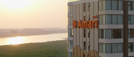 A modern building with a sign reading "Amari" and a view of a river at sunset.