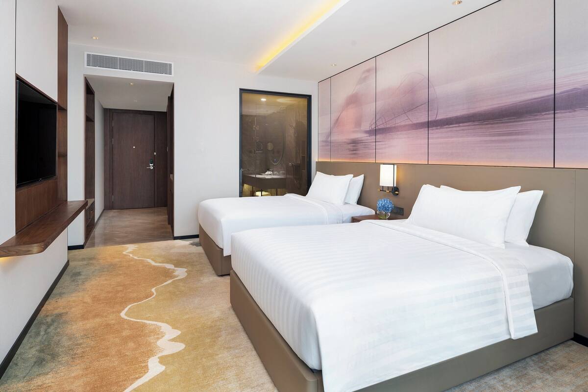 A hotel room with two beds, a TV, a large abstract painting, and a unique carpet design.