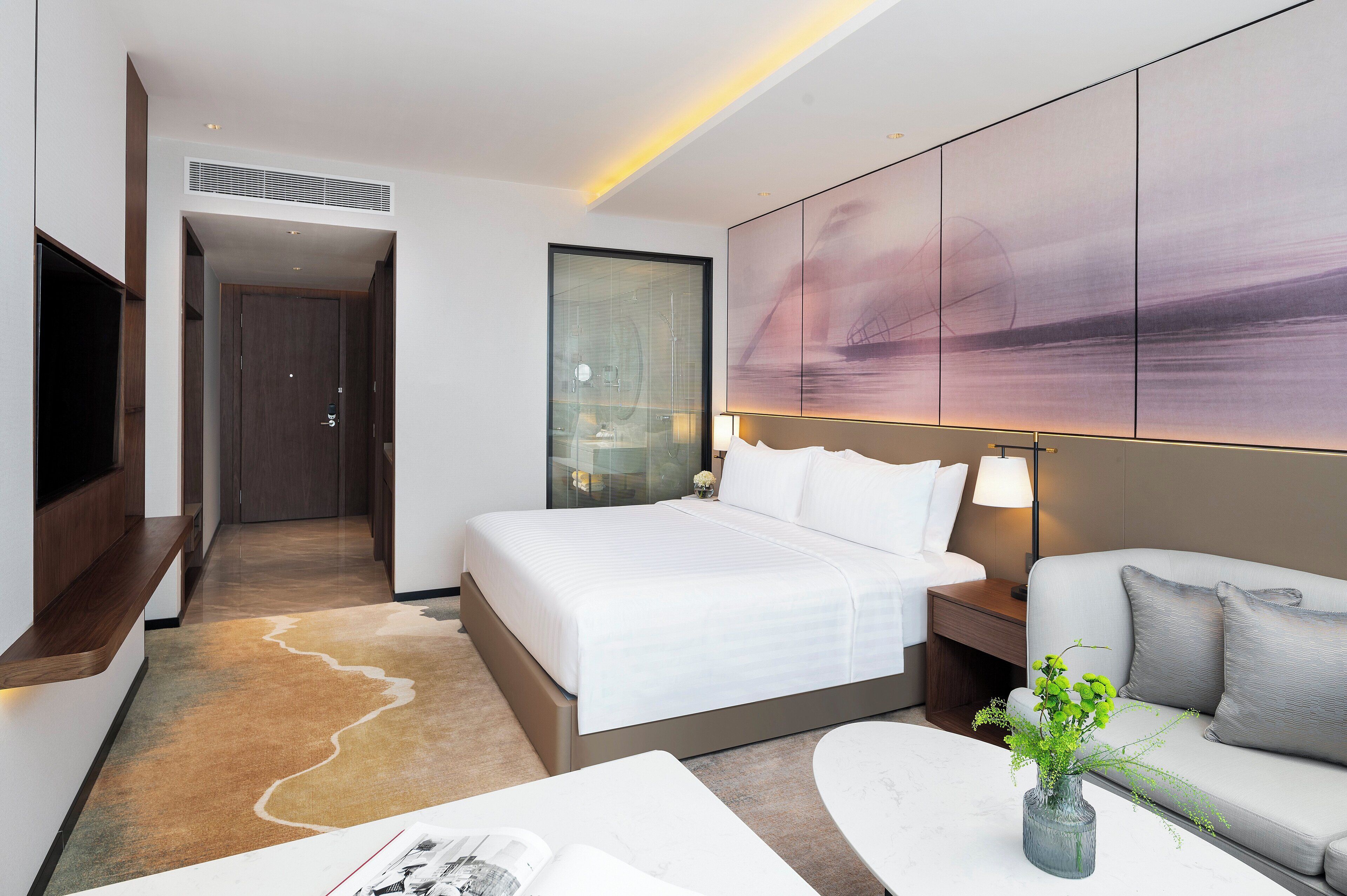 Une chambre d’hôtel moderne avec un grand lit, un canapé, une télévision et un tableau au mur.