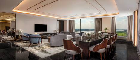A modern living room with a large TV, a dining area with a glass table, and a view of the outdoors.