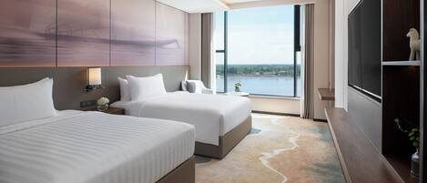 Een moderne hotelkamer met twee bedden, een groot raam met uitzicht op een waterlichaam en een flatscreen televisie op een houten dressoir.